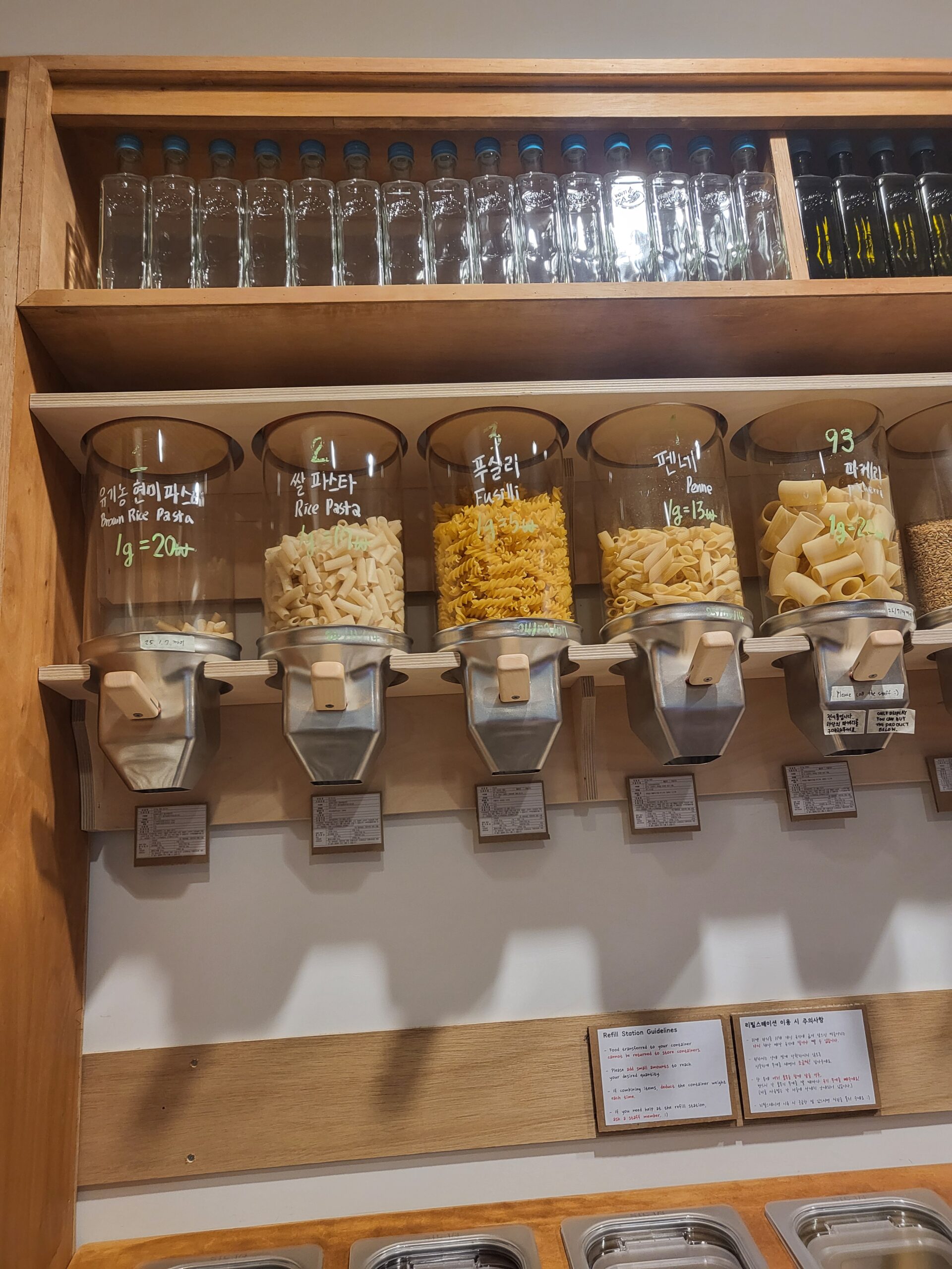 The refill station's gravity dispensers, filled with different pasta shapes, price per gram written by hand on each glass jar