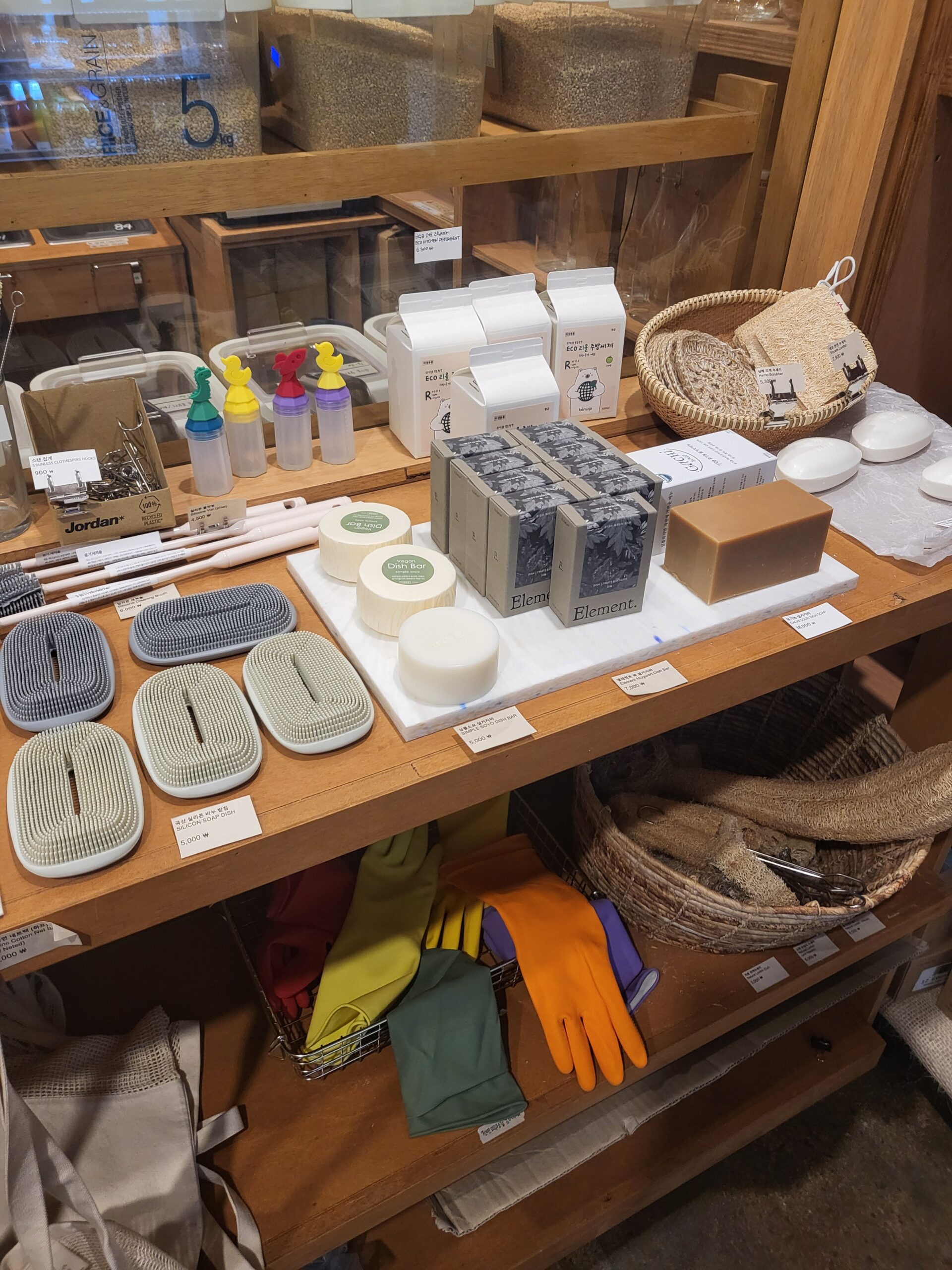 The eco household corner — natural loofahs, solid dish soap bars, silicone scrubbers, and a basket of reusable rubber gloves